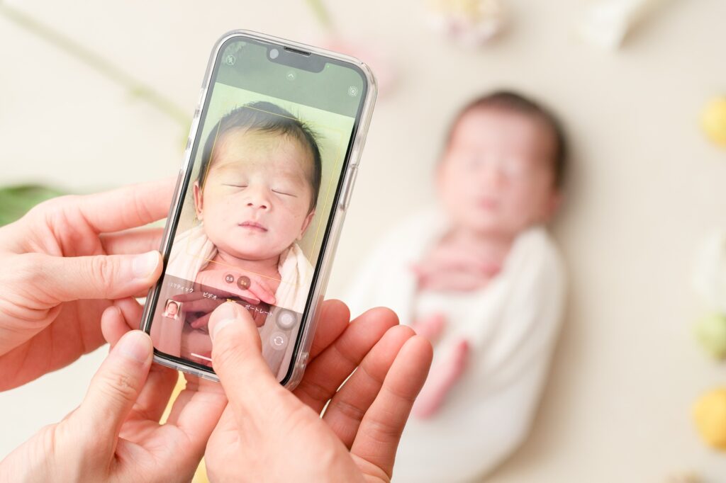 飯田市のニューボーンフォト出張撮影|スマートフォンで赤ちゃんを撮影するパパとママの様子の写真