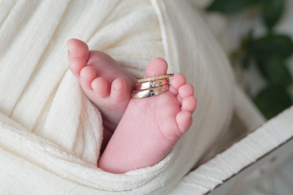 安曇野市でのニューボーンフォト|白いおくるみの赤ちゃんの足にパパとママの結婚指輪と婚約指輪の写真