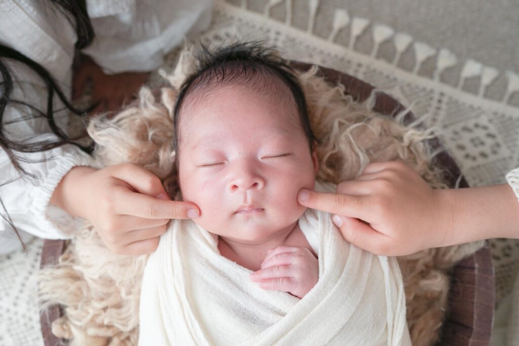 安曇野市でのニューボーンフォト|お兄ちゃんとお姉ちゃんが赤ちゃんのほっぺたに触れているの写真