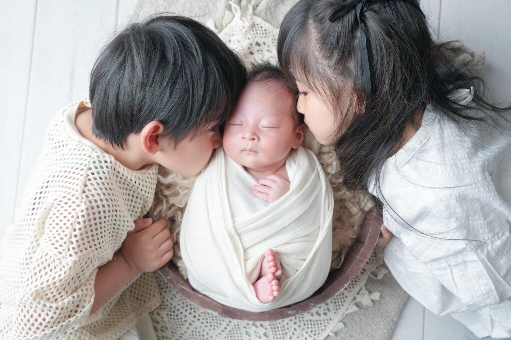 安曇野市でのニューボーンフォト|お兄ちゃんとお姉ちゃんが赤ちゃんにキスをしているの写真